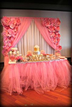 a table topped with pink flowers and cake next to a window covered in sheer tulle