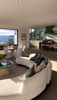 a living room filled with furniture next to a large glass window overlooking the ocean on top of a hill