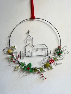 a christmas wreath hanging on the wall with a church in the background and holly decorations around it