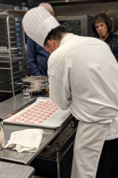 two chefs are working in the kitchen preparing doughnuts for baking and another man is looking on