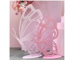 two pink butterfly sculptures sitting next to each other on top of a table with flowers in the background