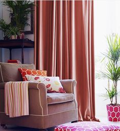 a living room with a chair, ottoman and potted plant in front of the window