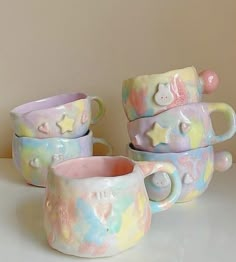 four ceramic mugs sitting on top of a white table next to each other and one has a teddy bear