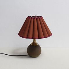 a lamp with a red shade on it sitting on a white table next to a wall