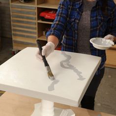 a woman holding a paintbrush in front of a white table