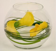 two yellow flowers are in a clear bowl with water and green stems on the side