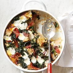 a dish with spinach, cheese and tomatoes in it next to a red spoon