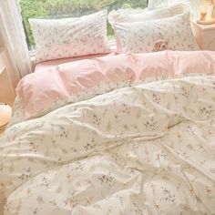 a bed with pink and white comforters in front of a window, next to a night stand