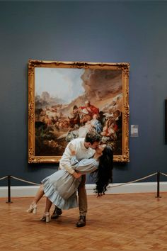 a man and woman are kissing in front of a painting on display at an art museum