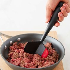 a hand holding a spatula in a pan filled with ground beef