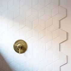 a white tiled wall with a gold shower faucet in the middle and a light shining on it