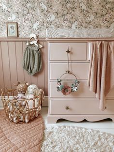 a baby's room with pink furniture and floral wallpaper, including a teddy bear in a basket