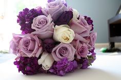 a bouquet of purple and white flowers sitting on top of a table next to a piano