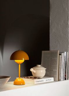 a yellow table lamp sitting on top of a white shelf next to a book and bowl