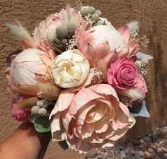 a hand holding a bouquet of flowers on top of a stone floored area next to a brown wall