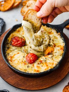 a person dipping some bread into a bowl of dip with tomatoes and cheese on top