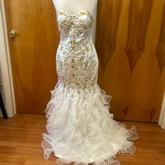 a white wedding dress with gold sequins on the bustle and skirt is displayed in front of a wooden door