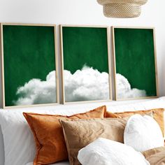 two green paintings on the wall above a bed with pillows and throw pillows in front of them