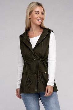 A versatile fashion piece that seamlessly blends style and utility. This vest boasts a convenient zipper and snap-button closure, ensuring ease of wear, while the adjustable drawstring waist provides a personalized, flattering fit. With practical pockets, it's a fashionable yet functional addition to any outfit, making it perfect for both casual and statement looks. Model is wearing a SmallModel SpecsHeight: 5'8"Bust: 34D Waist: 24"Hips: 37"*Color may vary slightly due to monitor resolutionMade Utility Outerwear With Functional Drawstring For Fall, Sleeveless Cargo Pocket Outerwear For Spring, Drawstring Outerwear For Fall Outdoor Activities, Fall Outerwear With Drawstring For Outdoor Activities, Casual Outerwear With Drawstring For Outdoor Activities, Hooded Vest With Pockets For Fall, Cotton Utility Jacket For Layering, Spring Outerwear For Outdoor Activities With Drawstring, Spring Drawstring Outerwear For Outdoor Activities