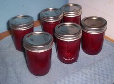 six jars filled with red liquid sitting on top of a blue towel next to a wall