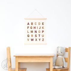 a teddy bear sitting next to a wooden table and chair in front of a framed alphabet poster