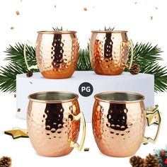 three copper mugs sitting on top of a white box next to pine cones and evergreen branches