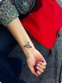 a woman's arm with a small tattoo on her left wrist and a red bag behind her