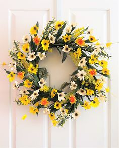 a wreath with yellow and white flowers hanging on a door