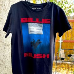 a blue t - shirt with the words bille eish on it hanging from a clothes rack