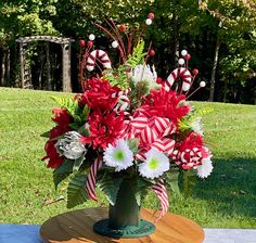 a vase filled with red and white flowers sitting on top of a wooden table in the grass