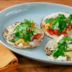 three tortillas on a blue plate with cilantro and avocado