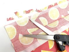 a pair of scissors cutting through fabric with lemons on the side and pink background