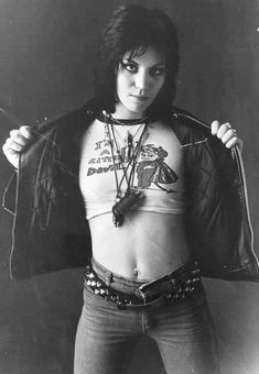 a woman with tattoos on her chest and leather jacket over her shoulders, holding a knife in one hand