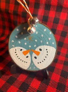 a wooden ornament with two snowmen on it sitting on a red and black checkered table cloth