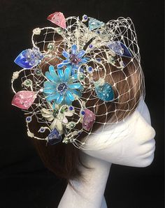 Delicate glass resin floral fascinator perfect for the guest who wants something unique and stunning. This design is a beautiful selection of glass effect leaves and flowers teamed with crystal swirls and set onto a fine base tiara band with a soft veiling finish. As with all our designs, this piece can be made exact to the image or in any colour combination to match in with your outfit. If a specific colour is required customers can message over an image of their outfit and accessories, or if t Whimsical Flower Fascinator For Parties, Whimsical Handmade Flower Headpieces For Party, Whimsical Party Headpiece With Handmade Flowers, Whimsical Handmade Hair Accessories For Wedding, Whimsical Flower Headpieces For Wedding, Whimsical Wedding Fascinator, Whimsical Flower Wedding Headpieces, Whimsical Blue Fascinator For Party, Blue Whimsical Wedding Headpiece