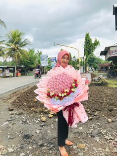 a woman holding a large bouquet of flowers on top of a dirt field next to a street