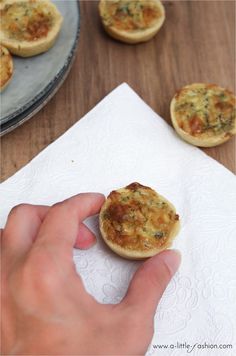 a hand is holding a small piece of food in front of some mini pizzas