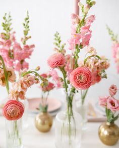 pink flowers in vases sitting on a table with plates and napkins behind them