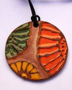 a close up of a necklace on a white surface with an orange and green leaf