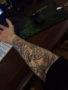 a person with tattoos on their arm is using a laptop and holding a cell phone