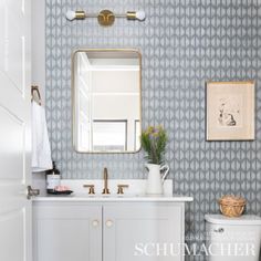 a bathroom with blue and white wallpaper, gold accents and a mirror above the sink