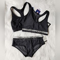 3 Piece Sporty Undie Set Champion Classic Sports Bra- Black On Black All-Over Logo Bra With Doubledry Technology, Chafe-Resistant Mesh Stripe Band, Compression For Reduced Or Eliminated Bounce. Racerback Style. Polyester/ Spandex. Calvin Klein Light & Stretchy Bralette & Boyshort Panty Set. Dark Gray/ Charcoal Fabric With A Soft Sheen Paired W/ Silver-Tone & Black, Wide, Striped Elastic Bands. Classic Ck Silhouettes- Similar To The Modern Cotton & Iron Strength Series. Size: All M New With Tags. Calvin Klein Sporty Activewear For Gym, Supportive Calvin Klein Activewear For Workout, Black Racerback Activewear For Loungewear, Calvin Klein Stretch Activewear For Yoga, Calvin Klein Black Activewear For Sports, Calvin Klein Black Activewear For Workout, Calvin Klein Black Workout Activewear, Calvin Klein Casual Activewear For Gym, Calvin Klein Medium Support Sports Bra For Workout