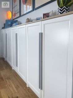 a kitchen with white cabinets and wood flooring next to two framed pictures on the wall