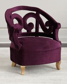 a purple chair with wooden legs and an ornate design on the armrests, in front of a white wall