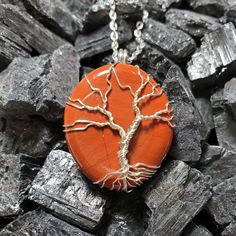 an orange pendant with a tree on it sitting on some rocks and silver chain necklace