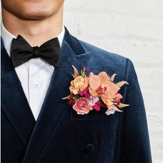 a man wearing a blue velvet suit and bow tie with flowers on the lapel