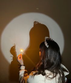 a woman holding a lit candle in front of a shadow of a person wearing a tiara