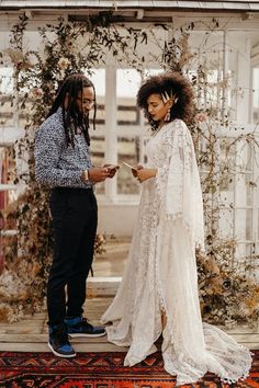 a man and woman standing next to each other in front of a flower covered wall