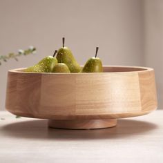 a wooden bowl filled with green pears on top of a table