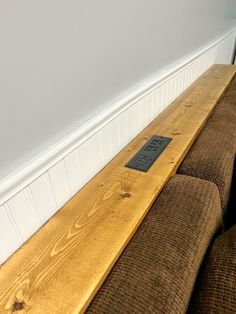 a wooden bench sitting in front of a white wall next to a brown couch with a black label on it